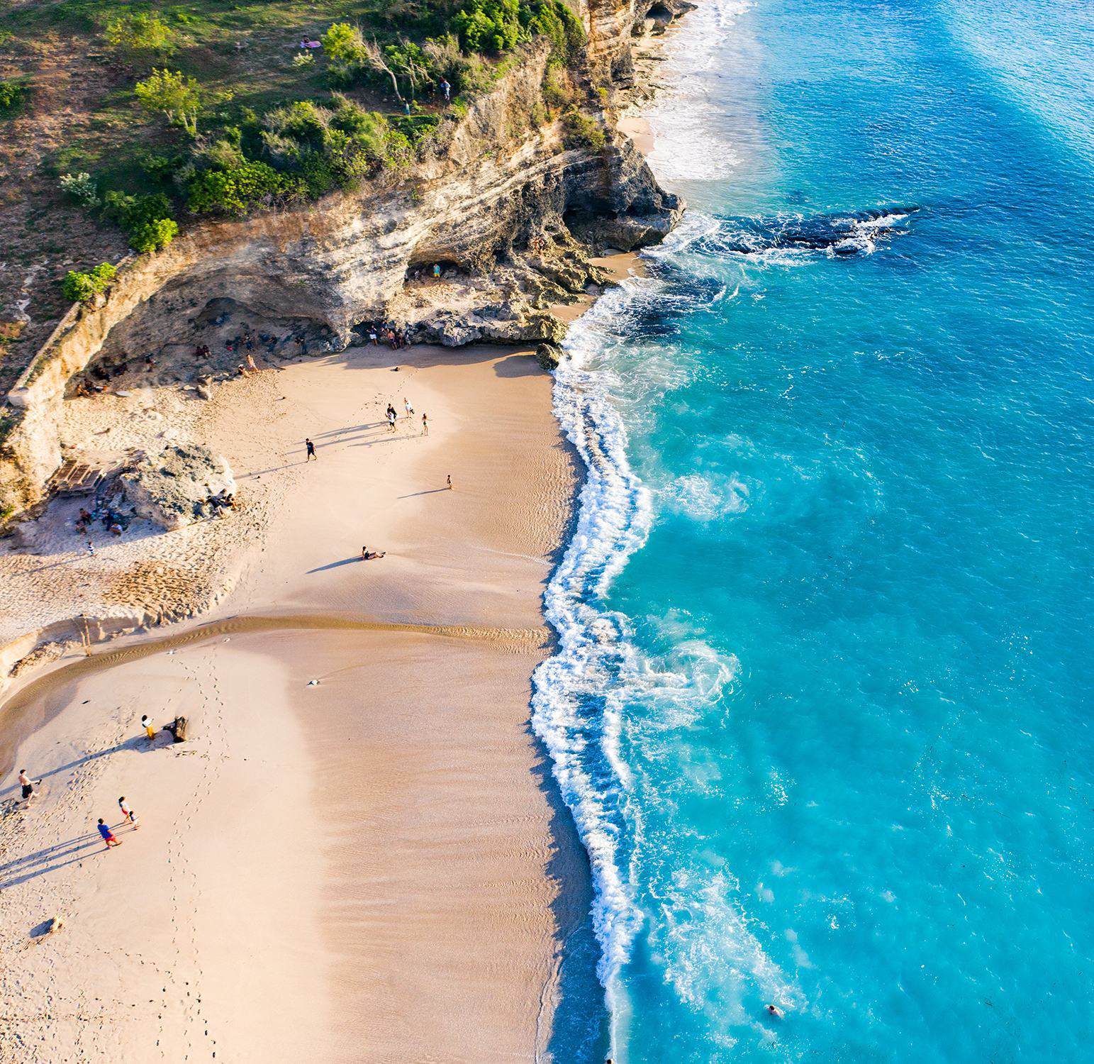 A white-sand cove below limestone cliffs on the Bukit coast, from the air