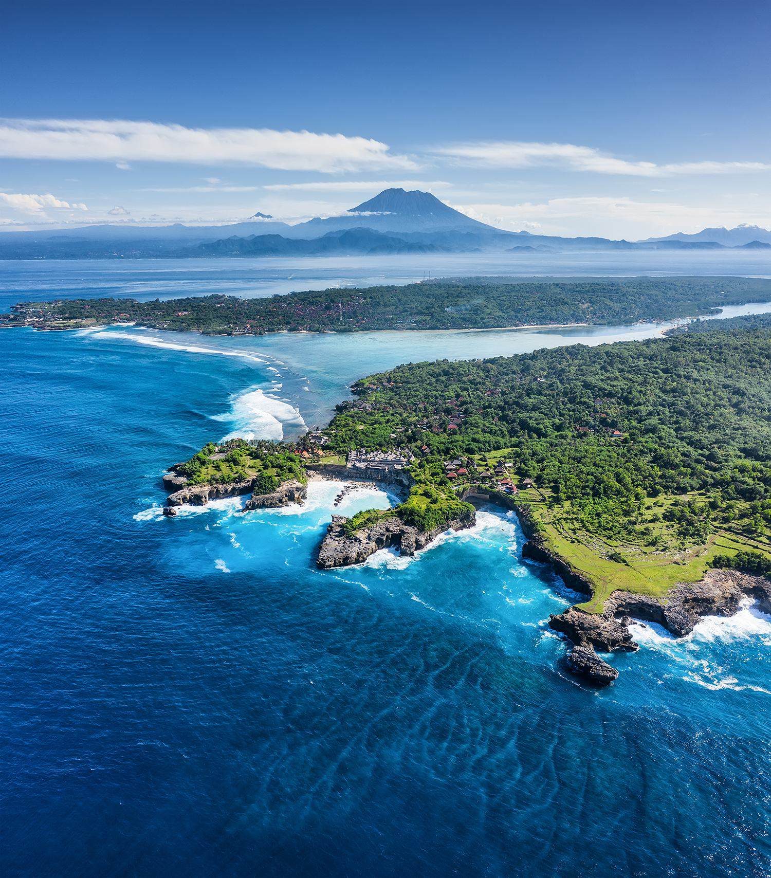 A rocky coastline with Mount Agung on the horizon, from the air